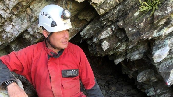 Der Höhlenforscher Stefan Voigt sitzt vor einem Höhleneingang und trägt einen Helm mit Stirnlampe. © Stefan Voigt 
