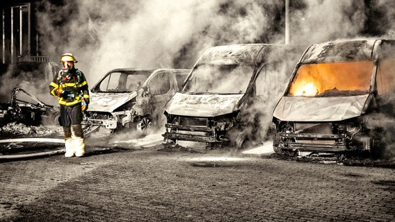 Ausgebrannte, bzw. brennende Kleintransporter bei einem Brand in Hamburg-Billbrook. Feuerwehrmann mit Atemschutzgerät am linken Bildrand. © picture-alliance 