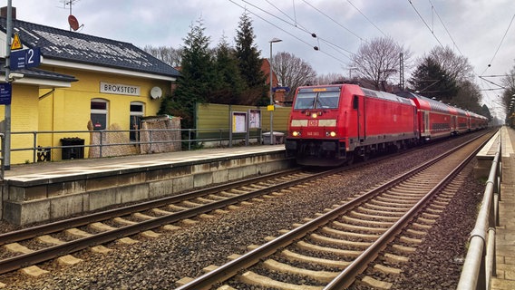 Blick über die zwei Gleise des Bahnhofs von Brokstedt in Richtung gelbes Bahnhofsgebäude. Ein Regionalexpress fährt gerade ein. © NDR Foto: Benedikt Severin Scheper