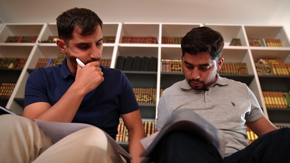 Ali Yain Karaca und Muhamed Memedi sitzen im Islamkolleg Osnabrück vor einem Bücherregal. © NDR 