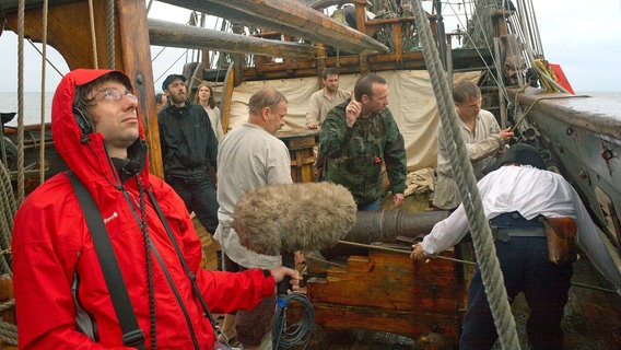 Regisseur Florian Dedio bei den Dreharbeiten auf einer historischen Fregatte. Es regnet - genau wie vor 300 Jahren, als die Seeschlacht vor Rügen tatsächlich stattfand. Regisseur Florian Dedio bei den Dreharbeiten auf einer historischen Fregatte. Es regnet - genau wie vor 300 Jahren, als die Seeschlacht vor Rügen tatsächlich stattfand. © NDR/Marcel Wollgast