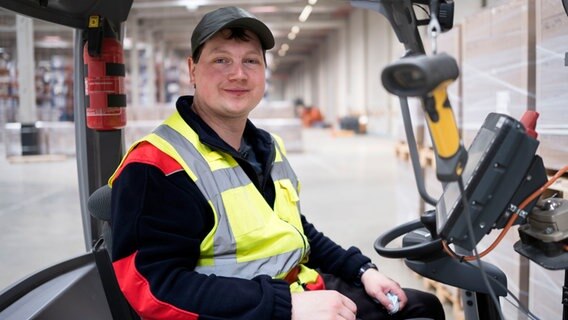 Timo Duderstadt sitzt lächelnd am Steuer eines Gabelstaplers und blickt in die Kamera. © NDR/dm film und tv produktion 