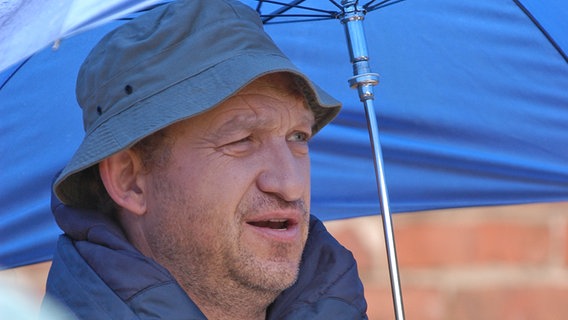 Neues aus Büttenwarder - Dreharbeiten Sommer 2007: Peter Heinrich Brix/Adsche sitzt während der Dreharbeiten unter einem blauen Regenschirm. © NDR/Nicolas Maack Foto: Nicolas Maack