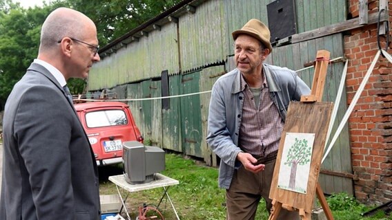 Zwei Männer blicken auf ein Bild auf einer Staffelei. Szene aus der 93. Büttenwarder-Folge "Kunst". © NDR/Nico Maack 