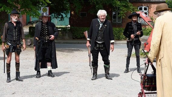 Szenenbild aus der 79. Büttenwarder-Folge "Sieben nach voll": Vier schwarz gekleidete und bewaffnete Männer stehen Onkel Krischan gegenüber. © NDR/Nicolas Maack Foto: Nicolas Maack