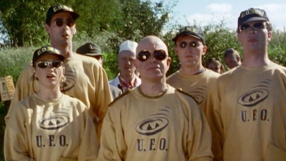 Szenenbild aus der 8. Büttenwarder-Folge "Ufos": Eine Truppe Ufo-Anhänger mit schrillen Ufo-Pullover. © NDR 