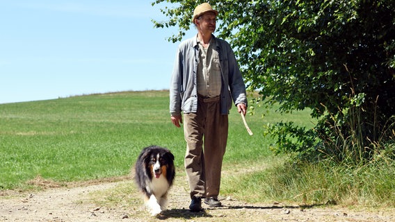 Szenenbild aus der 85. Büttenwarder-Folge "Verdammter Hund": Adsche geht mit einem Hund auf einem Feldweg. © NDR/Nico Maack Foto: Nico Maack