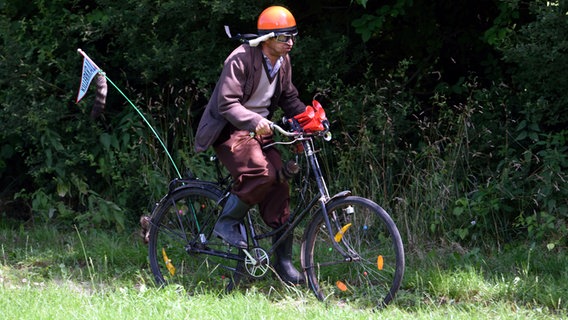 Szenenbild aus der 85. Büttenwarder-Folge "Verdammter Hund": Kuno fährt mit seinem Killerkralle-Fahrrad. © NDR/Nico Maack Foto: Nico Maack