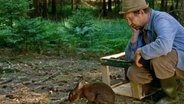 Dreharbeiten zu 61. Büttenwarder-Folge "Knopfhase": Adsche (Peterse Heinrich Brix) hockt vor einem Hasen. © NDR 