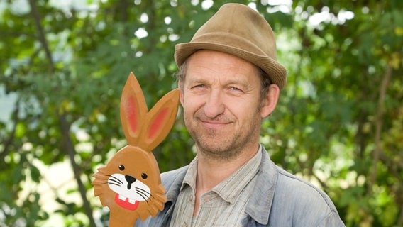 Szenenbild aus der 35. Büttenwarder-Folge "Ostern": Adsche mit einer Osterhasen-Holzfigur. © NDR/Nicolas Maack Foto: Nicolas Maack