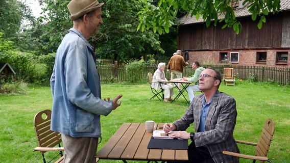 Szene aus der 95. Büttenwarder-Folge "Nur noch 21 Tage": Zwei Männer an einem Tisch im Garten. © NDR/Nicolas Maack 