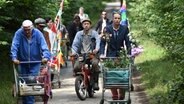 Szenenbild aus der 66. Büttenwarder-Folge "Rekord": Onkel Krischan schiebt einen Einkaufswagen den Feldweg entlang, gefolgt von jingen Männern. © NDR/Nicolas Maack Foto: Nicolas Maack