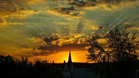 Die Sonne geht hinter eine Kirche unter und erzeugt eine Art Heiligenschein. © NDR Foto: Manfred Elsner aus Greifswald