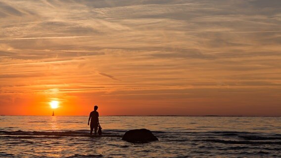 Ein Mensch steht während des Sonnenuntergangs im Wasser am Strand von Lubmin. © NDR Foto: Uwe Mahler aus Lubmin