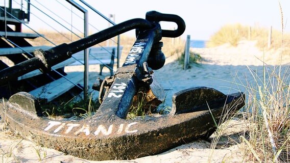 Ein Anker mit der Aufschrift "Titanic" liegt am Strand neben einem Rettungsturm. © NDR Foto: Anke Hanusik aus Grimmen