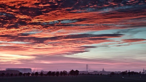 Über der Rügenbrücke erstreckt sich eine Wolkendecke in den Farben rot und blau. © NDR Foto: Hartmut Heidrich aus Stralsund