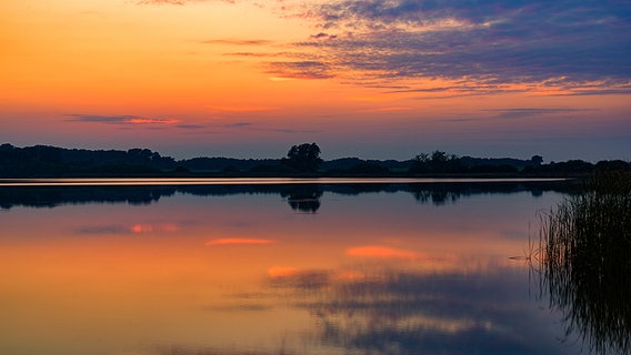 Der orangefarbene Abendhimmel spiegelt sich in einem See. © NDR Foto: Gerhard Volkmann aus Tessin