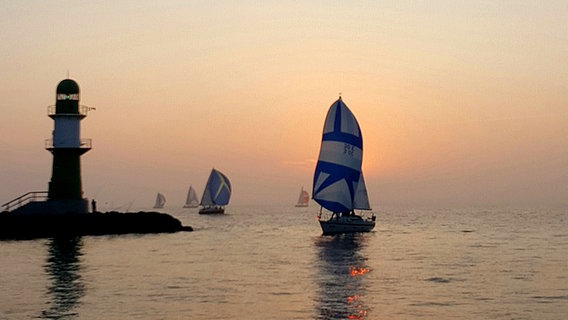 Blick auf einen Leuchtturm und auf einige Segelboote im Meer bei Sonnenuntergang. © NDR Foto: Andreas Erdt aus Dummerstorf