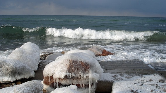 Auf einen vereisten Steinstrand rollt eine Welle zu © NDR Foto: Martin Scholwin aus Warnemünde