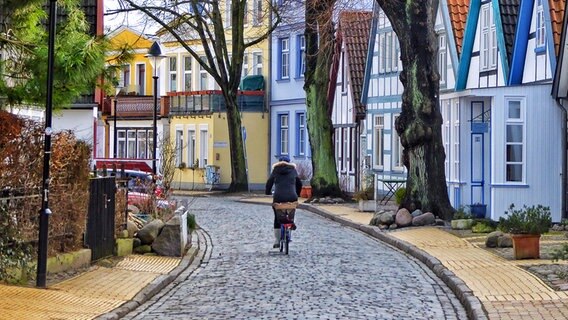 Eine Fahrradfaherin auf einer Straße zwischen farbigen Häusern. © NDR Foto: Richard Lotz aus Rostock