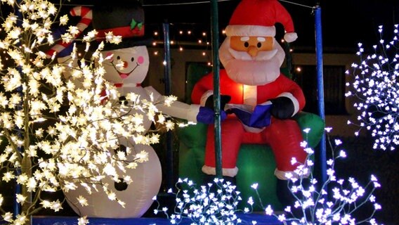Eine Weihnachtsmannfigur und ein Schneemann stehen nebeneinander unter einer Lichterkette. © NDR Foto: Eckhard Wolfgramm aus Salow