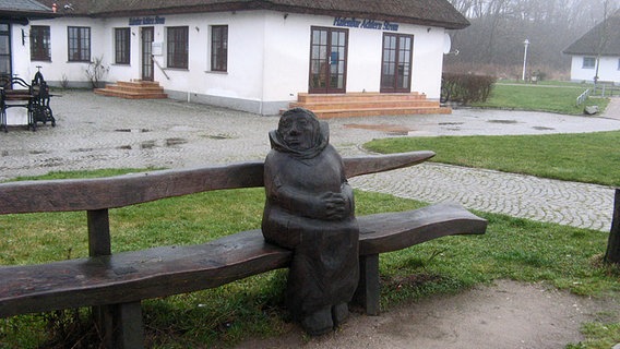 Eine Holzstatue sitzt einsam auf einer Bank vor der Hafenbar von Kloster. © NDR Foto: Christine Arendt aus Kloster