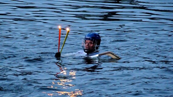 Ein Schwimmer in Eishockeyoutfit mit Fackeln im Wasser © NDR Foto: Eckhard Wolfgramm aus Salow