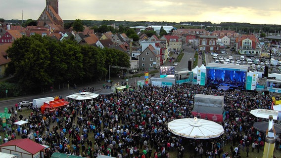 Hunderte Menschen stehen auf einem Platz vor einer bunt beleuchteten Bühne (Luftbild). © NDR Foto: Kurt Obst aus Barth