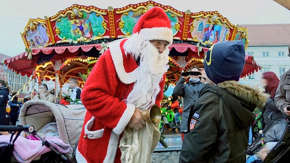 Weihnachtsmann steht mit einem kleinen Jungen vor einem Karussell auf dem Weihnachtsmarkt. © NDR Foto: Helmut Kuzina aus Wismar