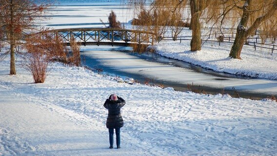 In der verschneiten Umgebung des Schweriner Sees steht eine Frau und fotografiert eine Brücke. © NDR Foto: Arnold Prosch aus Schwerin