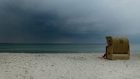Ein Strandkorb steht am Strand vor einer dunklen Wolkenwand. © NDR Foto: Helmut Kuzina aus Wismar
