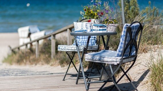 Zwei Gartenstühle und ein Tisch mit Blumen in einer Vase stehen an einem Strandzugang © NDR Foto: Michael Weise aus Damshagen