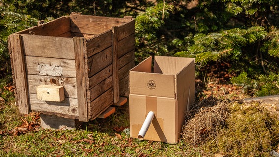 Ein Holzkasten und eine Pappkiste stehen auf einer Wiese. © NDR Foto: Udo Tanske