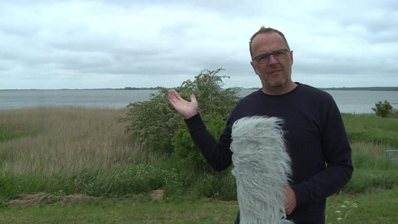 Stefan Kreibohm steht mit einem Mikrofon vor einem Strand © NDR 