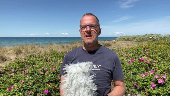 Stefan Kreibohm steht mit einem Mikrofon vor Sträuchern. © NDR 