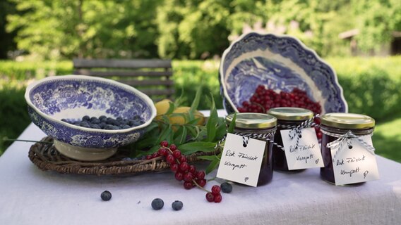 Gläser mit Beeren-Kompott stehen auf einem mit Heidelbeeren und Johannisbeeren dekoriertem Tisch. © NDR Foto: Paul Knoll