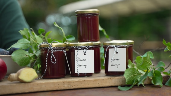 Jars of plum ketchup stand on a wooden board.  © NDR Photo: Paul Knoll