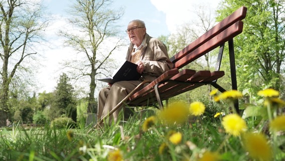 Der 95-jährige Leo Thiel sitzt auf einer Parkbank und hat ein Buch in seinen Händen. © NDR 