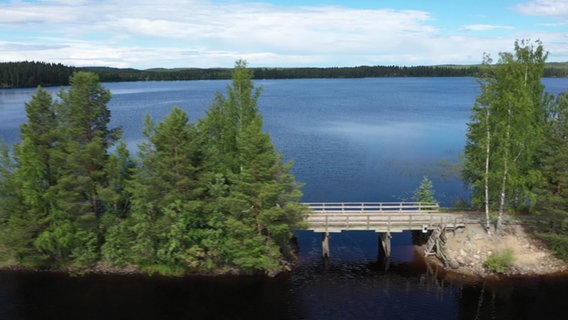 Ein großer See, im Vordergrund sind zwei kleine Inseln zu sehen, verbunden durch eine kleine Brücke. © NDR / Lisa Knittel 