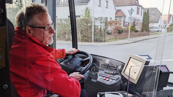 Eins Busfahrer sitzt auf dem Fahrersitz und lenkt den Bus. © NDR Foto: Screenshot