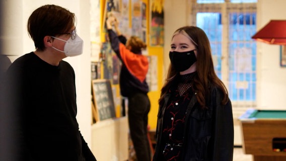 Ein Mädchen mit schwarzem Mundschutz steht in einem Gebäude © NDR Foto: Screenshot