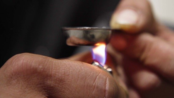 Eine Metalllöffel wird mit einem Feuerzeug erhitzt. © NDR Foto: Screenshot