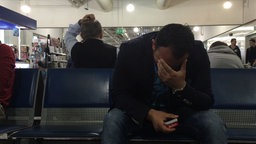 Rami wartet am Flughafen und hält sich die Hand vor sein Gesicht. © NDR Foto: NDR