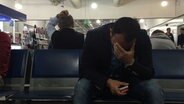 Rami wartet am Flughafen und hält sich die Hand vor sein Gesicht. © NDR Foto: NDR