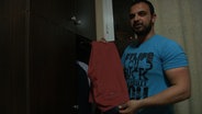 Rami zeigt in einem Hotelzimmer eine neue Hose. © NDR Foto: NDR