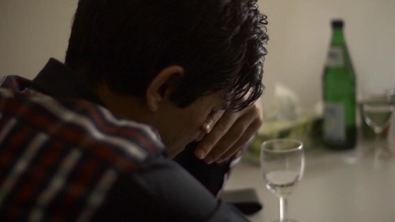 Ein junger Flüchtling sitzt am Tisch und hält sich die Hand vors Gesicht  