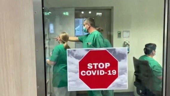 Ein "Stop-Covid"-Schild auf einer Tür, im Hintergrund Pflegekräfte © NDR Foto: Screenshot