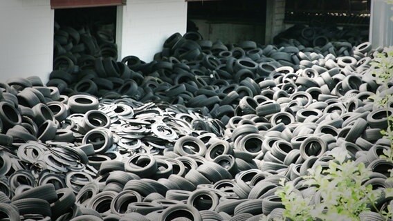 Tausende von Reifen liegen auf einem Haufen neben einem weißen Gebäude. © NDR Foto: Screenshot