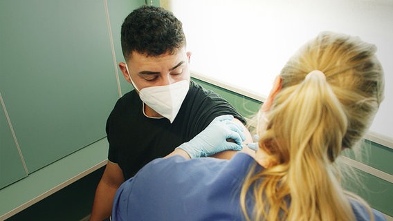 Ein Mann mit Mundschutz bekommt eine Spritze in den Arm von einer Krankenschwester  