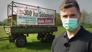 Ein Mann mit Mundschutz neben einem Protest-Plakat gegen die Errichtung eines Solarparks  